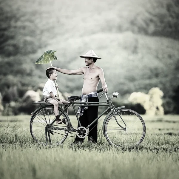 A local Thai man and his son smiling at each other while riding an old bike through a rice field in the rain, showcasing the authentic joy of rural Thai life.