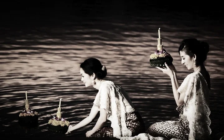 two beautiful thai women in thai traditional dress release krathong into the rever on Loy Krathong festival