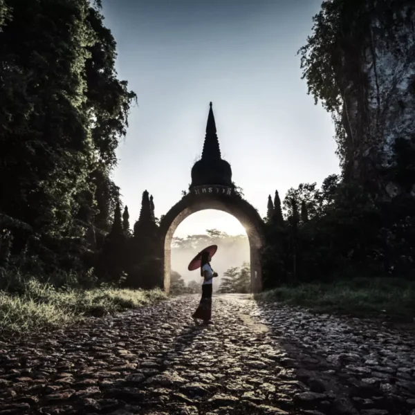 thai lady in tradional thai dress holds an umbrella at the temple gate- ultimate Thailand hidden gems.
