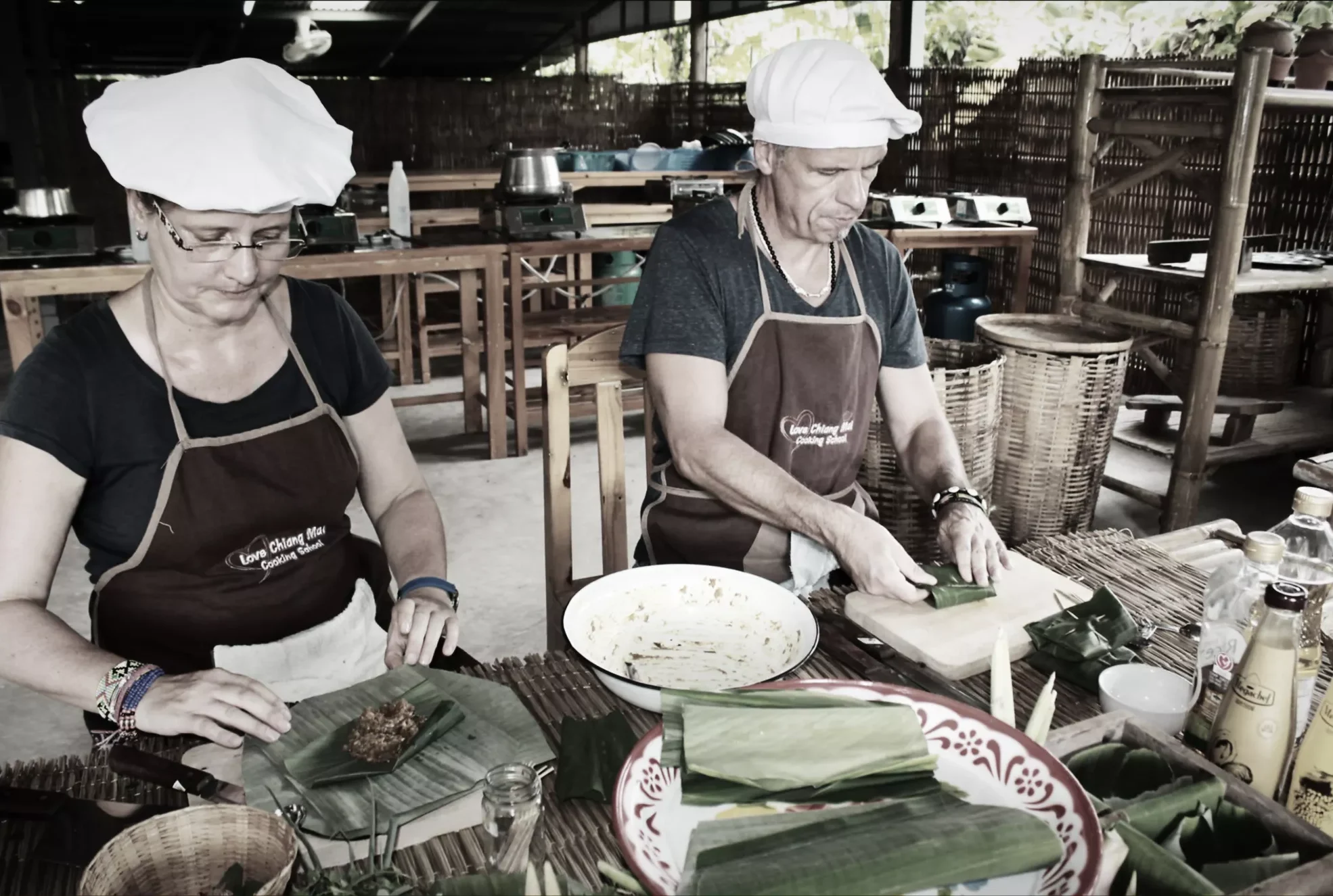 a couple learn how to wrap a banana leave over fish curry