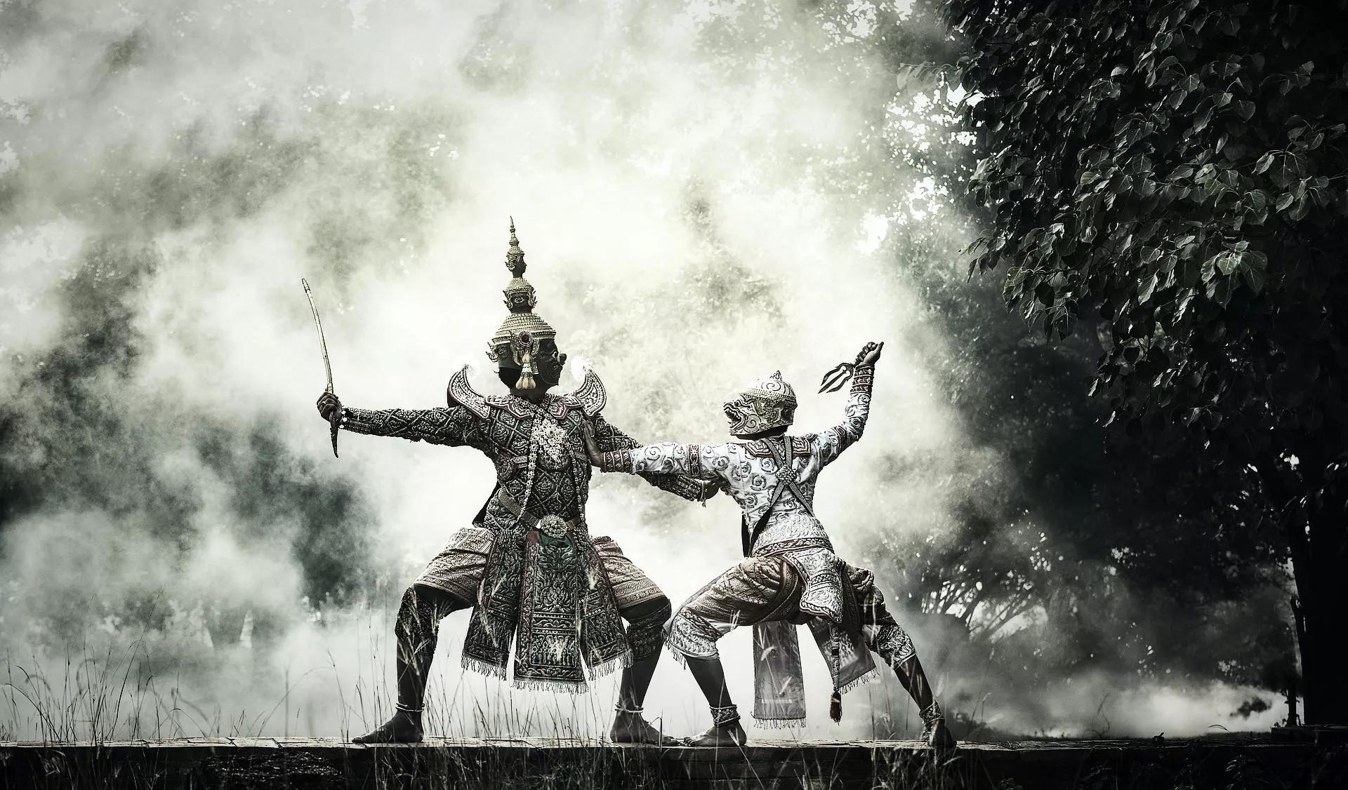 Two Thai Khon dancers in traditional costume performing outdoors in dramatic mist and light. Ultimate Authentic Thailand Travel to witness.