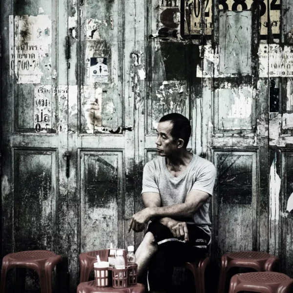 Thai local man relaxing on red plastic chair. Unbothered.